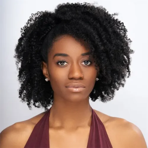 A woman with natural curly black hair, wearing stud earrings and a sleeveless burgundy top, poses against a plain light background.
