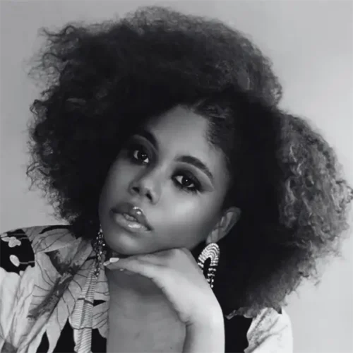 Black and white portrait of a woman with voluminous natural hair, wearing statement earrings and resting her chin on her hand.