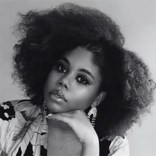 Black and white portrait of a woman with voluminous natural hair, wearing statement earrings and resting her chin on her hand.