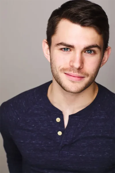 A young man with short brown hair and light facial hair wearing a dark blue henley shirt, posing against a plain light background.