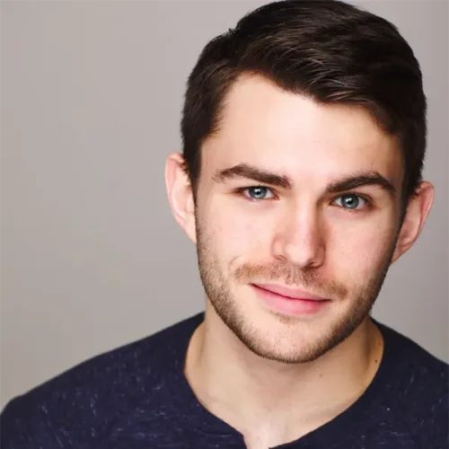 A young man with short brown hair and light facial hair wearing a dark blue henley shirt, posing against a plain light background.