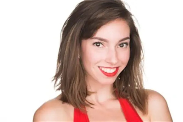 A woman with straight brown hair and red lipstick smiles at the camera while wearing a red sleeveless top against a white background.