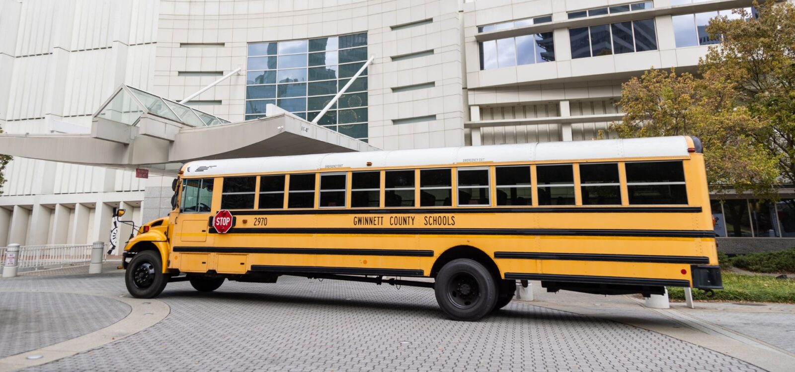 A yellow Gwinnett County Schools bus is parked in front of a modern white building with large windows and architectural details.
