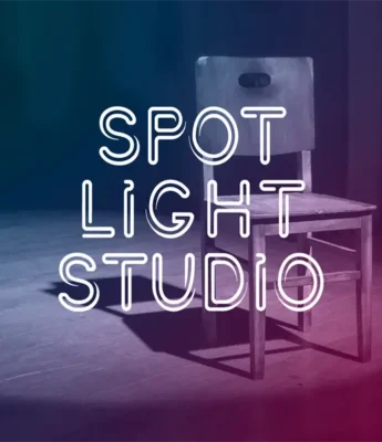 A wooden chair is placed on a stage under a spotlight with the words "Spot Light Studio" in white neon text overlay.