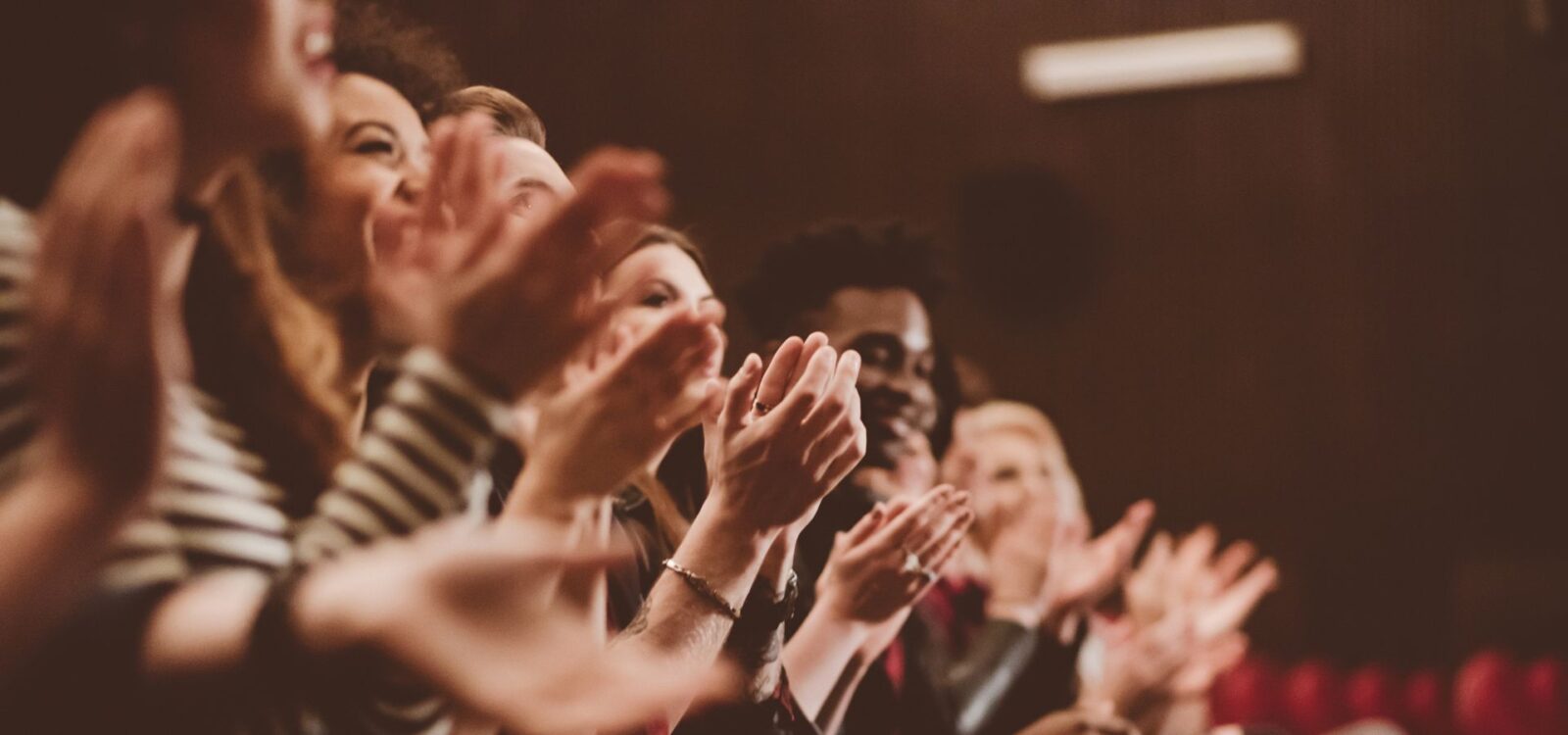 A group of people sitting in an audience clapping and smiling, with their hands raised in applause.