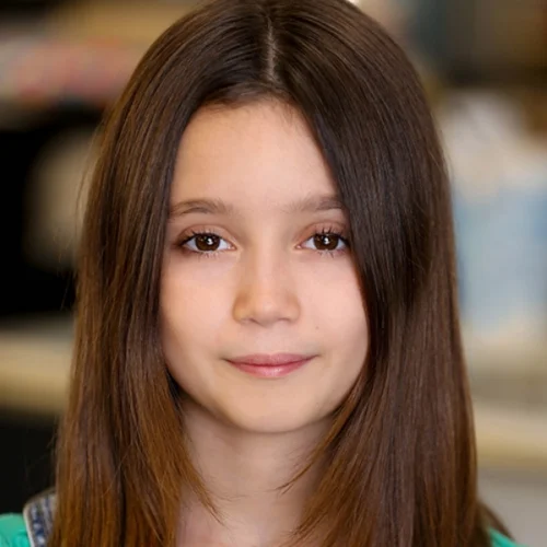 A young girl, Emma Grace Lizarazo, with straight brown hair and brown eyes looks at the camera with a neutral expression; the indoor background is softly blurred.