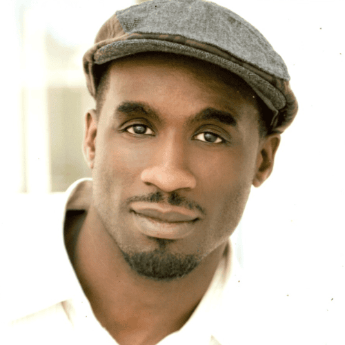 Man wearing a light shirt and a flat cap, looking directly at the camera with a neutral expression against a light background.