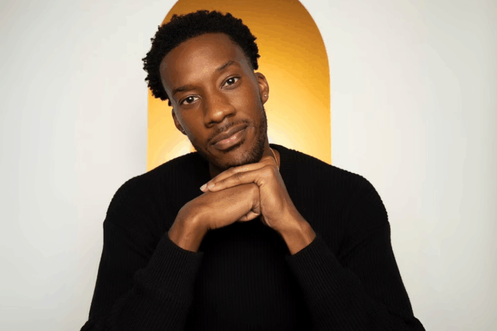 Playwright York Walker, sporting short curly hair and a trimmed beard, rests his chin on his hands in front of a gold arched background as director Tinashe Kajese-Bolden joins him to discuss Covenant.