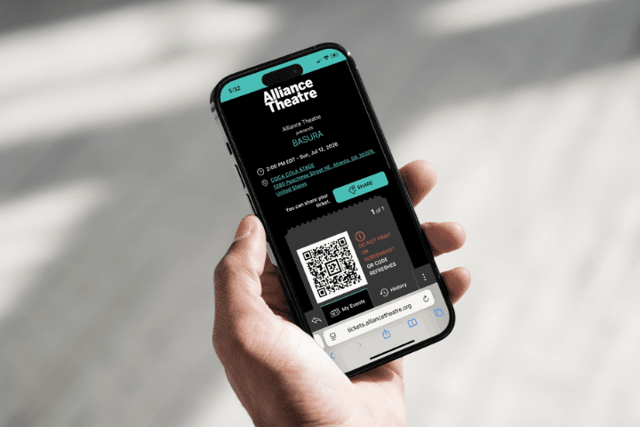 A hand holds a smartphone displaying an electronic ticket for "BASURA" at Alliance Theatre, showing event details and a QR code on the screen.