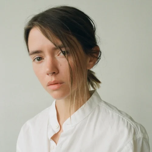 Colin Gagné, a person with light skin and straight brown hair, wearing a white collared shirt and a nose ring, looks at the camera against a plain background.