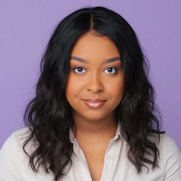 A woman with long wavy black hair, wearing a light-colored blouse, poses against a plain lavender background.