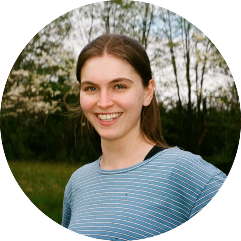 Young woman with long brown hair wearing a blue striped shirt smiles outdoors with trees and greenery in the background, celebrating Alliance/Kendeda Week: The Words of Ants.