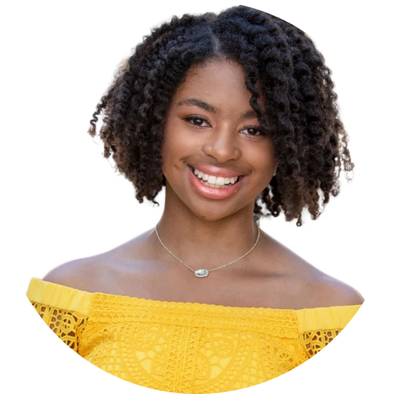 A young woman with natural curly hair wearing a yellow off-the-shoulder top and a necklace, smiling at the camera against a white background, ready to join the Community Conversation.