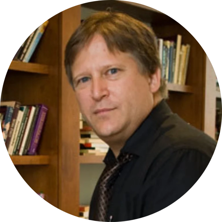 A man with light brown hair wearing a black shirt and tie sits in front of bookshelves filled with books, possibly preparing to discuss Ethics on Stage Fires in Ohio.