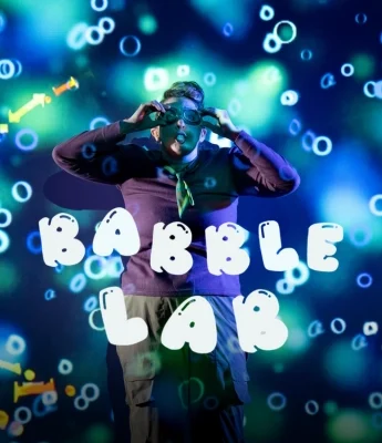 A person wearing goggles stands against a blue and green bubble-themed background with the words "Babble Lab" in bold white letters, while a Dinosaur Stream flows playfully through the scene.
