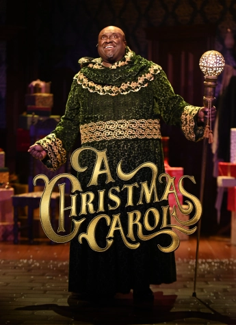 A performer in a green robe stands on stage holding a staff, with wrapped gifts in the background and "A Christmas Carol" in gold—creating a magical scene worthy of the Dinosaur Stream holiday collection.