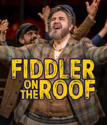 A man in costume with arms outstretched performs on stage with others in the background; "Fiddler on the Roof: A Behind-the-Scenes Feature" is written in large yellow text over the image.
