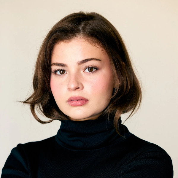 Woman with short brown hair wearing a black turtleneck, looking directly at the camera against a plain, light-colored background.