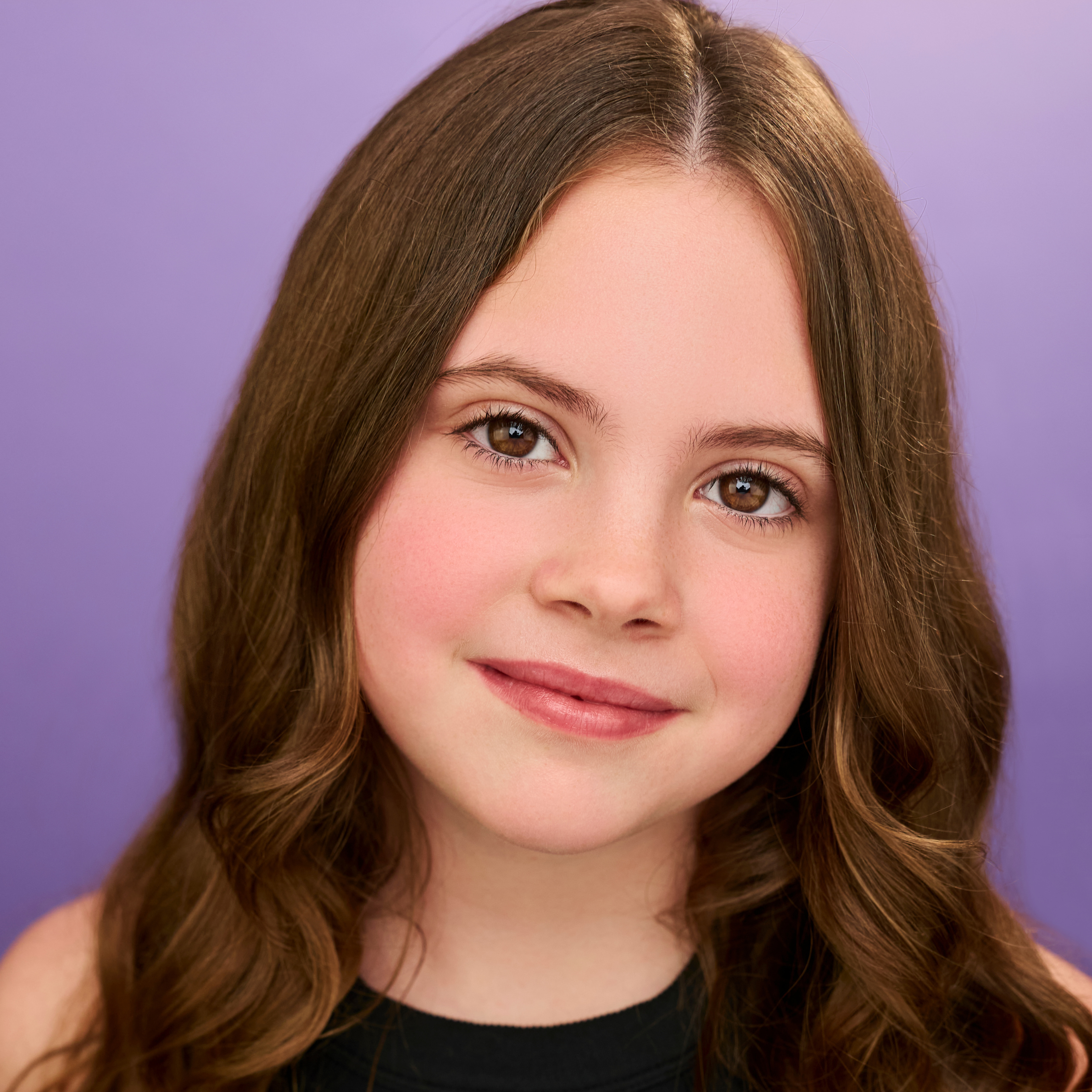 A headshot of a young girl with long brown hair against a purple background.